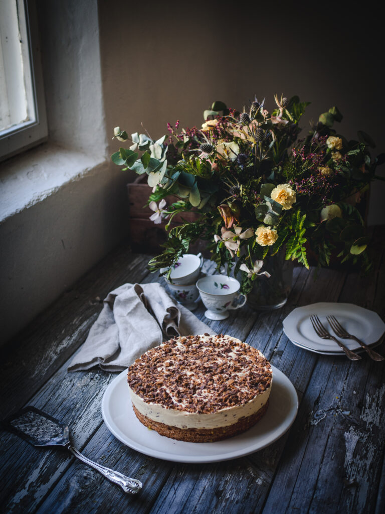 I’m not sure there is anything dreamier than a homemade daimiskake “Daim ice cream cake”. The base is a macaron bottom that’s sweet and soft with a chewy texture of almonds. The ice cream is a heavenly concoction of heavy cream, sugar, and egg yolks with a subtle hint of coffee and vanilla all encasing pieces of crunchy Daim candy bars. To top it all off, even more of that delightful chocolate toffee is sprinkled on top. Each bite has a burst of textures and perfectly balanced flavors. 

The star of this dessert is Daim, a milk chocolate-covered almond toffee that’s perfectly crunchy. Daim was created by the Marabou company, based in Sweden, as a version of the American Heath Bar. It was launched under the name of “Dajm” in 1953 in Norway and Sweden, quickly becoming a national favorite. It was then launched the following year in Finland, and in 1971 it arrived in Denmark before making its way to the UK, France, and Germany. In 1990, it was renamed as Daim in most of the countries it was in and by 2005, the UK and Ireland also made the change. 

While Daim has its inception at the Marabou factory in Sweden, its roots go back to the Norwegian chocolate manufacturer Freia. Freia was founded by Olaf Larsen and Fredrik Wilhelm Hjorth Christensen in 1889. Ten years later, Johan Throne Holst took over the management of the company from Larsen and led it to a commercial success, with Freia being the leading Norwegian brand in sweets. 
In 1916, based on the success in Norway, the Throne-Holst family founded a chocolate factor in Sweden. Due to a trademark conflict, the name Freia/Freja could not be used, so Marabou was chosen as a representation of the marabou stork featured as part of Freia’s logo at the time. 
Today, Daim is enjoyed on its own and in desserts, like this classic Daimiskake. As we celebrate Norway’s Constitution Day on the 17th May and join in on other festivities in the month, this ice cream cake is sure to make an appearance. Make it in the morning, ready for the evening or prepare it advance. If you can’t access Daim bars, substitute with Heath bars or another chocolate toffee bar. 
